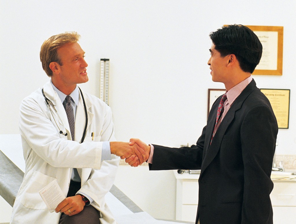 Doctor and businessman shaking hands in clinic