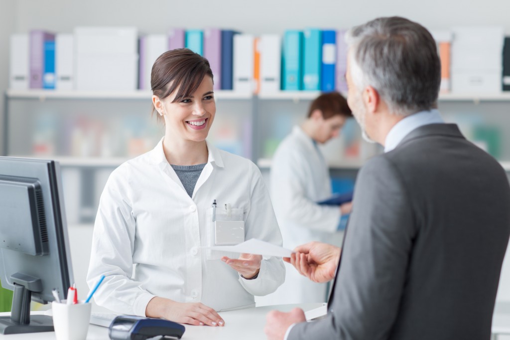 Male customer at the pharmacy, he is giving to the smiling pharmacist a prescription, healthcare concept